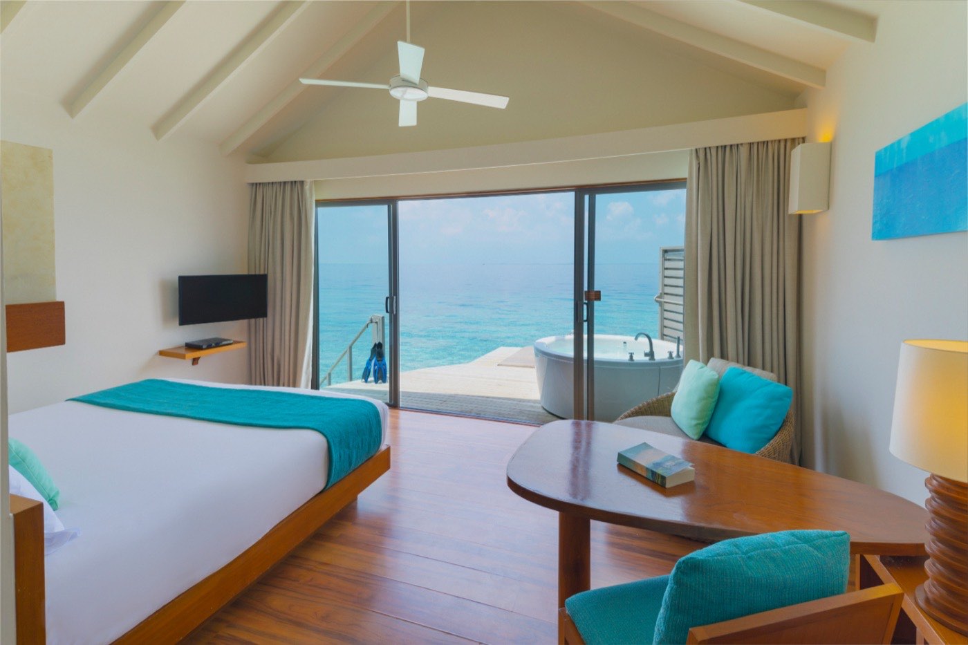An overwater villa deck with sun loungers above clear shallow water.